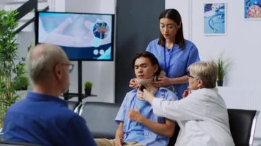 Hastane bekleme odasında muayene sırasında yaralı hastaya boyun tasmasını çıkarmasında yardımcı olan doktor. Boyun yaralanması geçiren Asyalı bir adam tıbbi personelden yardım alıyor
