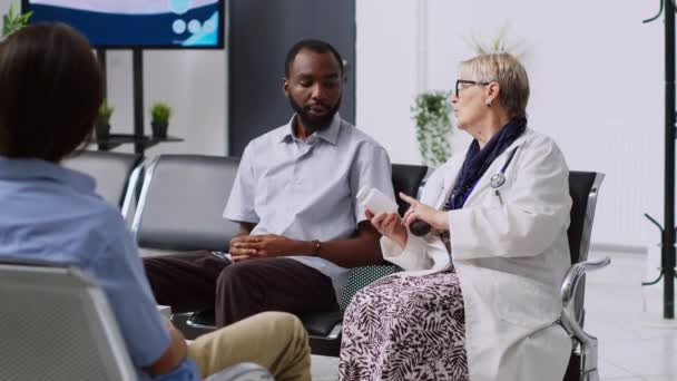 アフリカ系アメリカ人患者に抗生物質ボトルを示す高齢者医療 病院の受付での検査中の医療専門知識を説明します 医者は病気の男と医療の治療を議論 — ストック動画