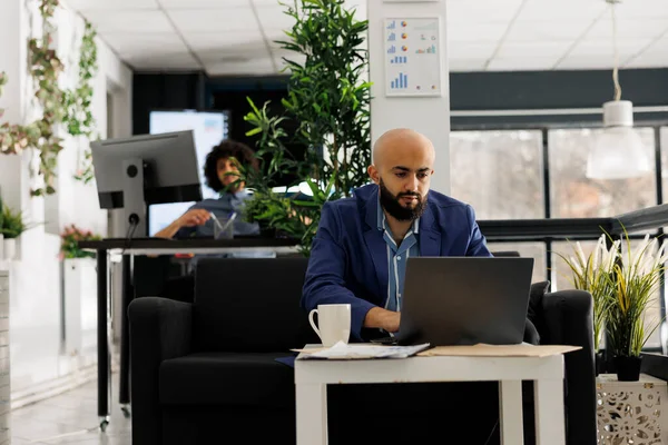 Arab business entrepreneur working at marketing data management on laptop in open space modern office. Start up executive manager solving job task while typing on computer