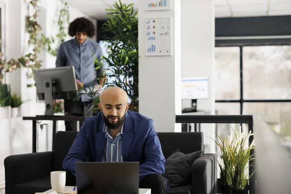 阿拉伯公司员工与公司办公室的远程团队讨论视频创业问题 在开放空间使用笔记本电脑与同事进行在线交流的年轻企业家 — 图库照片