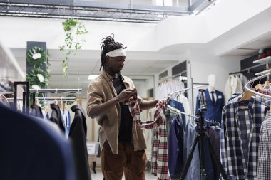 Akıllı telefondan video kaydedilirken mağazadaki giyim markası hakkında konuşan Afrikalı bir Amerikalı. Sosyal medya moda blogcusu tişörtünü gösteriyor ve online takipçiler için eleştiri yapıyor