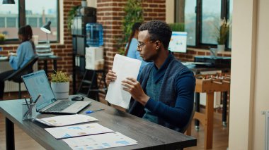 Afrika kökenli Amerikalı yönetici dosyaları inceliyor, iş istatistiklerini okuyor ve birlikte çalışma alanında yıllık sonuçlar elde ediyor. Bilgisayarda online verilerle çalışan erkek çalışan, geliştirme raporlarını kontrol ediyor.