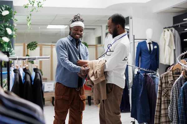 笑顔の男がシャツを着て 店内の営業担当者とファッショントレンドを議論しています アシスタントとチャットしながらブティックでモダンな服を着てアフリカ系アメリカ人のショッピングモールの顧客 — ストック写真