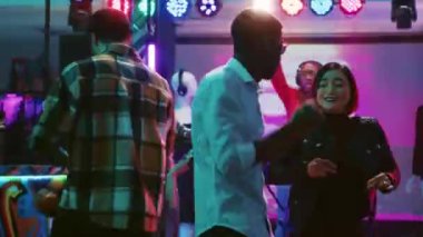 Çeşitli arkadaşlar canlı müzik eşliğinde dans ediyorlar. Gece kulübünde dans pistinde neşeli hissediyorlar. Gençler diskotekteki performanslarıyla eğleniyorlar sahne ışıkları altında acayip dans hareketleri yapıyorlar. Üçayak atışı.