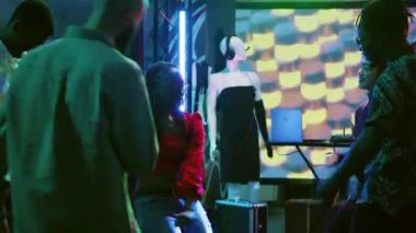 Çeşitli insanlar kulüpte elektronik müzik eşliğinde parti yapıyorlar ve DJ sahnede dans pistinde zıplıyorlar. Eğlenen ve eğlenen mutlu insanlar, disko ışıkları. Üçayak atışı.