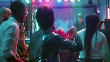 Çılgın DJ sahneye atlıyor, ritimleri karıştırıyor, gece kulübündeki insanlarla eğleniyor. Genç erkekler ve kadınlar birlikte eğleniyor ve elektronik müzik eşliğinde dans ediyorlar. El kamerasıyla..