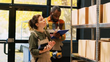 İşçi takımı, stokları kontrol ediyor. Depoda mallarla birlikte çalışıyorlar. Kadın ve erkek, kağıt ve tabletteki üretim mallarının listesini inceliyor. El kamerasıyla..