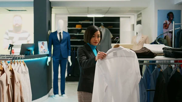 アジアの女性は 店舗のハンガーで正式なシャツをチェックし 新しいファッションコレクションブランドを購入します 流行の商品 衣料品店をしようとするショッピングセンターモールを訪れる女性のクライアント — ストック写真