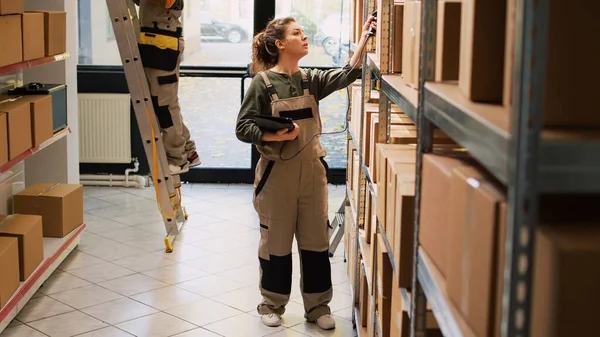 stock image Woman manager working on stock inventory with tablet scanner, verifying barcodes of products in packages. Female worker analyzing boxes with cargo goods in storage room depot.