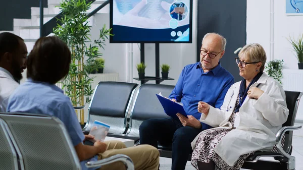 Medyk Siedzący Krześle Recepcji Szpitalnej Wyjaśniający Diagnozę Choroby Starszemu Pacjentowi — Zdjęcie stockowe