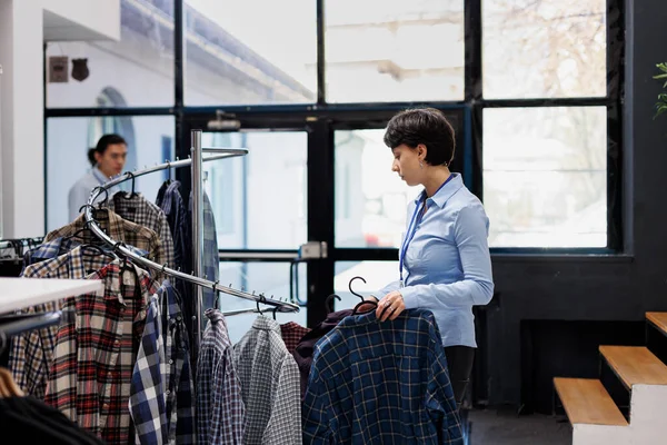 Stylish manager preparing store for opening, arranging fancy clothes on hangers in shopping mall. Caucasian woman looking at fashionable merchandise, checking price in modern boutique