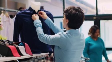 Çalışan manken için resmi tişört ayarlıyor, modern butik görüntüde çalışıyor. Alışveriş merkezi müdürü modaya uygun ürün ve aksesuarları kontrol ediyor, giyim mağazasında yeni moda koleksiyonu