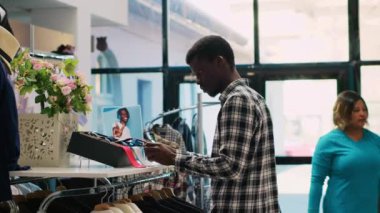 Afro-Amerikan müşteri kravat kontrol malzemeleri, şık aksesuarlar ve giyim mağazasından alışveriş. Modern butikte yeni moda koleksiyonu olan bir müşteri rafa bakıyor.