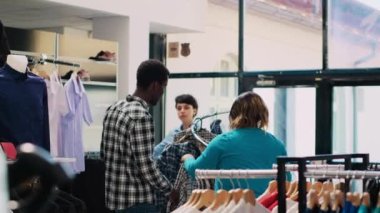Afrika kökenli Amerikalı çift şık gömleklere bakıyor, modern butikte moda ürünlerle dolu askıları kontrol ediyorlar. Neşeli müşteriler giyim mağazasından almadan önce kıyafet malzemelerini kontrol ediyorlar.