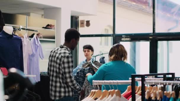 非洲裔美国人夫妇看着时髦的衬衫 检查衣架上摆满了现代精品店的时髦商品 在服装店购买服装之前 顾客们会很高兴地查阅服装材料 — 图库视频影像