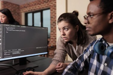 Teknik mühendis Html kodu için uygulama tasarımcısından yardım istiyor, terminal penceresindeki veritabanı betiğine işaret ediyor. Ajansında uygulama geliştirme programı üzerinde çalışan programcı mühendisler..