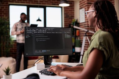 Ev oturma odasında uzaktan çalışan programcının programlama dili metniyle bilgisayar ekranına seçici odaklanma. Erkek arkadaşı dizüstü bilgisayar kullanırken Afrikalı Amerikalı kodlayıcı bilgisayarda kod geliştiriyor.