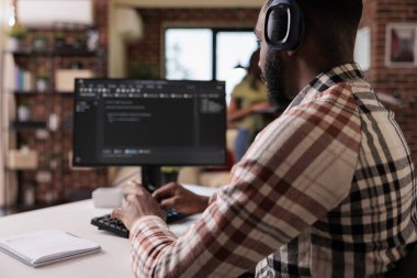 Kablosuz kulaklıklı Afrikalı Amerikalı programcı kişisel bilgisayarda kod yazarken müzik dinliyor. Freelance kodlayıcısı kulaklıktaki çevrimiçi radyodan keyif alırken yazılım geliştiriyor.