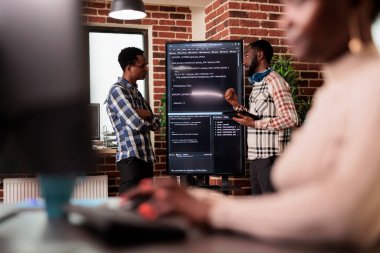 Html kodunu analiz eden programcı mühendisler büyük ekranın önünde duruyor, yapay zeka projesindeki hataları kontrol ediyorlar. Yazılım geliştiricileri bu ajansta makine öğrenme yazılımı üzerinde çalışıyorlar.