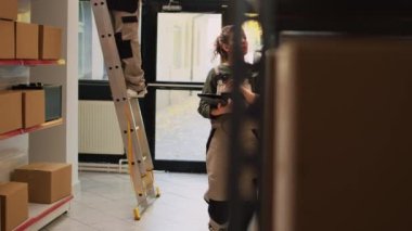 Tablet tarayıcıyla lojistik üzerinde çalışan kadın denetçi kutulardaki barkodları kontrol ediyor. Depo deposunda stok ürünleriyle paketleri inceleyen kadın çalışan..