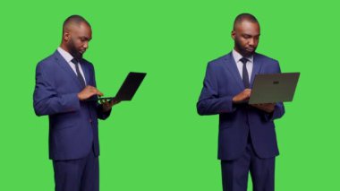 Ofisteki genç adam stüdyoda dizüstü bilgisayarda çalışıyor ve kablosuz bilgisayarla sosyal medya uygulamalarına bakıyor. Taşınabilir bilgisayar, yeşil ekran arkaplanı olan internet sitesi kullanan şirket çalışanı.