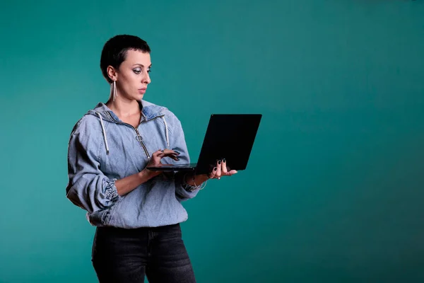 stock image Confident woman holding laptop computer typing business strategy working at financial project in studio with isolated background. Positive female collaborating with remote colleagues