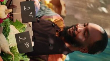 Dikey video: Çeşitli satıcı ve müşteri ürünleri kutuya koymayı seçiyor, çiftçi ev yapımı eko meyve ve sebze satıyor. Genç satıcı ve yaşlı müşteri renkli biyo-üretime bakıyor. El bilgisayarı