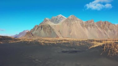 Okyanusla buluşan dev dağ zinciri, siyah kumlu görkemli İzlanda manzarası. Kuzeyli Stoksnes yarımadası, Vestrahorn dağları ve doğal manzaralı rotası var. El kamerasıyla..