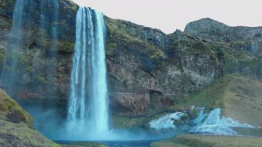 Görkemli seljalandsfoss şelalesi, tepeden aşağı akan güzel su. İskandinav çağlayanı, dağları ve kayalıkları olan İskandinav manzarası. El kamerasıyla..