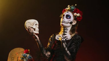 La Cavalera Catrina, Meksika cadılar bayramı geleneğini kutlamak için stüdyoda kafatasıyla konuşuyor. Korku kostümü içinde vücut sanatıyla Noel Baba Muerte. El kamerasıyla..