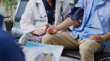 Kıdemli doktor Asyalı hastayla kardiyoloji muayenesi yapıyor. Kan ve nabız ölçümü yapıyor. Doktor, hastane lobisindeki tıbbi tonometreyi kullanarak adamın hipertansiyonunu ölçüyor.