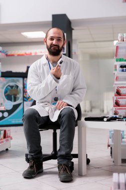 Eczacı, eczaneye gelen müşterileri beklerken parmaklarının nabzını ölçen tıbbi oksimetre kullanıyor. İlaç ürünleri, vitaminler ve takviyelerle dolu bir sağlık merkezi.