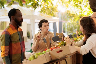 Genç müşteriler çiftçi pazarında bedava yiyecek tadıyorlar, taze meyve ve sebzeler dışarıda. Erkek ve kadın yerel taze organik pazarlardan sağlıklı ürünler satın alıyorlar..