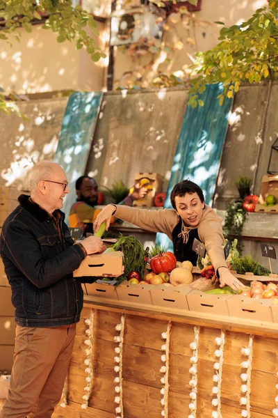 向销售新鲜生物天然产品的当地农民微笑 向老顾客提供粮食市场水果和蔬菜 女摊贩与老年男子谈论季节性各种健康产品 — 图库照片