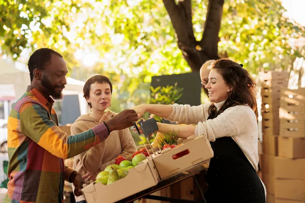 卖主向顾客提供样品 同时在当地农民市场上销售本地种植的水果和蔬菜 年轻的多种族家庭夫妇在参观食品展销会时品尝天然有机产品 — 图库照片