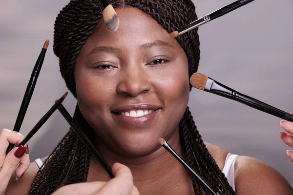 用专业的刷子在女人脸上涂上装饰性化妆品的艺术家手 美容师手臂做自然的面部化妆 让笑着的美籍黑人模特特写镜头 — 图库照片
