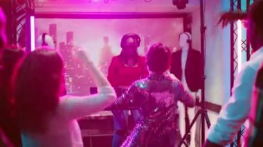 Kadın DJ gece kulübünde müziği karıştırıyor, dans pistinde çeşitli insanlarla parti yapıyor. Çılgın kız diskotekte disko partisinde eğleniyor, kulüp sahnesinde ses istasyonu var. El kamerasıyla..