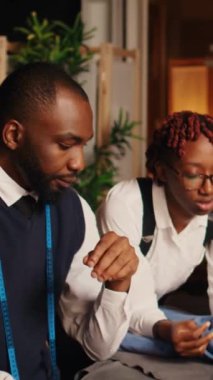 Dikey video Afrikalı Amerikalı terziler, terzilik aletleri ve ekipmanlarıyla lüks moda koleksiyonu yapmak için kumaş seçiyorlar. Erkek ve kadın tasarımcılar malzemeler ve el sanatları ile çalışıyorlar..