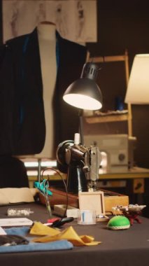Dikey video boş lüks terzi atölyesi. Dikiş dikmek ve yeni moda kıyafet koleksiyonu yapmak için kullanılan aletler. Giysi imalatında kullanılan kumaş ve iş istasyonları ile atış yapan firma..