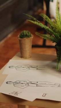 Elbise eskizleriyle dikey video dikiş atölyesi ve kağıt üzerinde moda öğeleri, el yapımı tekstil endüstrisi aletli atölyesi. Özel dikim kıyafetler için çizimlerle dolu boş bir atölye. Kapat..