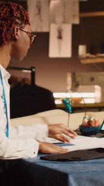 Atölye atölyesinde çizimi inceleyen dikey video Afrikalı Amerikalı terzi yeni özel yapım kıyafetler tasarlamak için tasarım modelini kontrol ediyor. El yapımı tekstil endüstrisinde çalışan kadın tasarımcı. El bilgisayarı