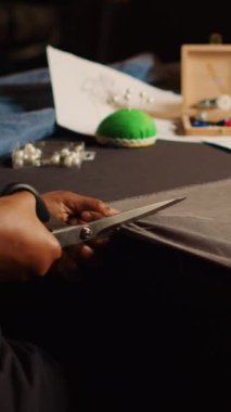 İş yerinde kumaş kesen dikey video Afrikalı Amerikalı öğrenci, malzeme hazırlamak ve dikiş dikmek için makas kullanan atölye öğrencisi. Endüstriyel aletlerle moda tasarım koleksiyonu yapan bir kadın