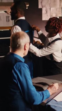Dikey video terzileri müşterinin vücudunu ölçüyor, atölyede özel moda koleksiyonu yapıyor. Deneyimli bir zanaatkar ve kadın mükemmel bir takım tasarlamak için ölçü alıyorlar. El bilgisayarı