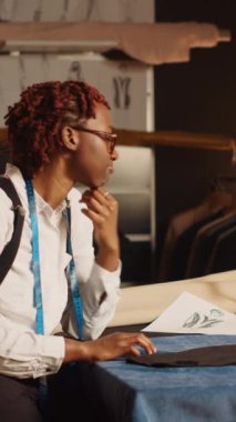 Dikey video terzisi, tablet üzerinde taslak veya çizimler kullanarak modern araçlarla moda tasarımı üzerinde çalışarak kıyafet yaratıyor. Endüstriyel atölyede giyim markası tasarlayan kadın çalışan.