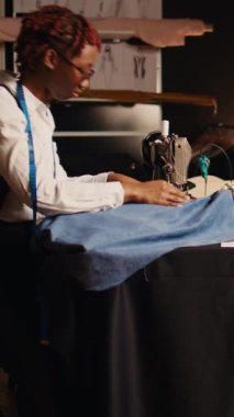 Dikey video tasarımcısı dikiş makinesinde çalışıyor. İş yerinde, profesyonel terzide giysi üretiyor. Genç modacı atölyede özel yapım kıyafetler yapmak için terzilik ekipmanı kullanıyor..