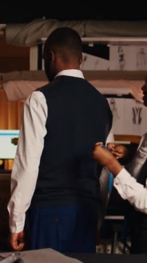 Dikey video tasarımcıları müşteri için ölçü alıyorlar, atölyede çalışıp özel yapım kıyafetler yapıyorlar. Üst düzey terzi ve çalışan ölçüm müşterisi mükemmel uygun giyim ürünleri tasarlamak için