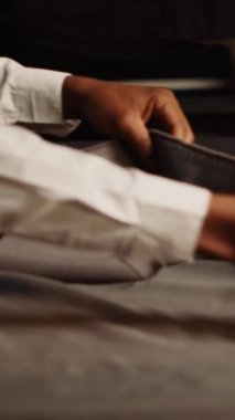 Modern kıyafetler yaratmak için dikey video terzisi ve asistan kumaş seçiyor, atölyede moda koleksiyonu için kıyafet hazırlıyor. İki tasarımcı malzeme seçiyor, el yapımı. El kamerasıyla.