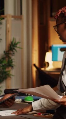 Atölyede tartışan dikey video ekibi yeni kıyafetler yaratmak için model ve taslak seçiyor. Tasarımcı ve asistan atölyede el işi aletleri kullanarak giyim markası üretiyorlar. El bilgisayarı