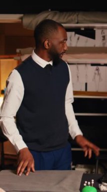 Atölyeye dikey video müşteri ceketi sığdırıyor. Mükemmel boyutta. Deneyimli terzi ve asistan, atölyede uygun ölçülere sahip lüks kıyafetler üretiyor. El bilgisayarı