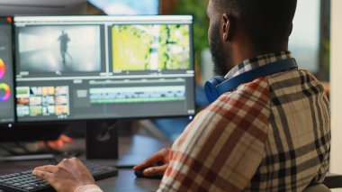 Genç grafik tasarımcısı, odaklı ışıklandırma ve renk derecelendirme kullanarak yazılım üzerinde video içeriğini düzenliyor. Erkek film yapımcısı pc multi monitörlerinde montaj üzerinde çalışıyor, görüntü yönetmeni.